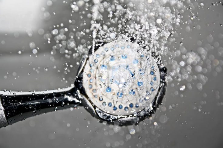Close-up of a showerhead spraying water with droplets suspended in the air, gray tones with blue accents, dynamic and fresh mood.
